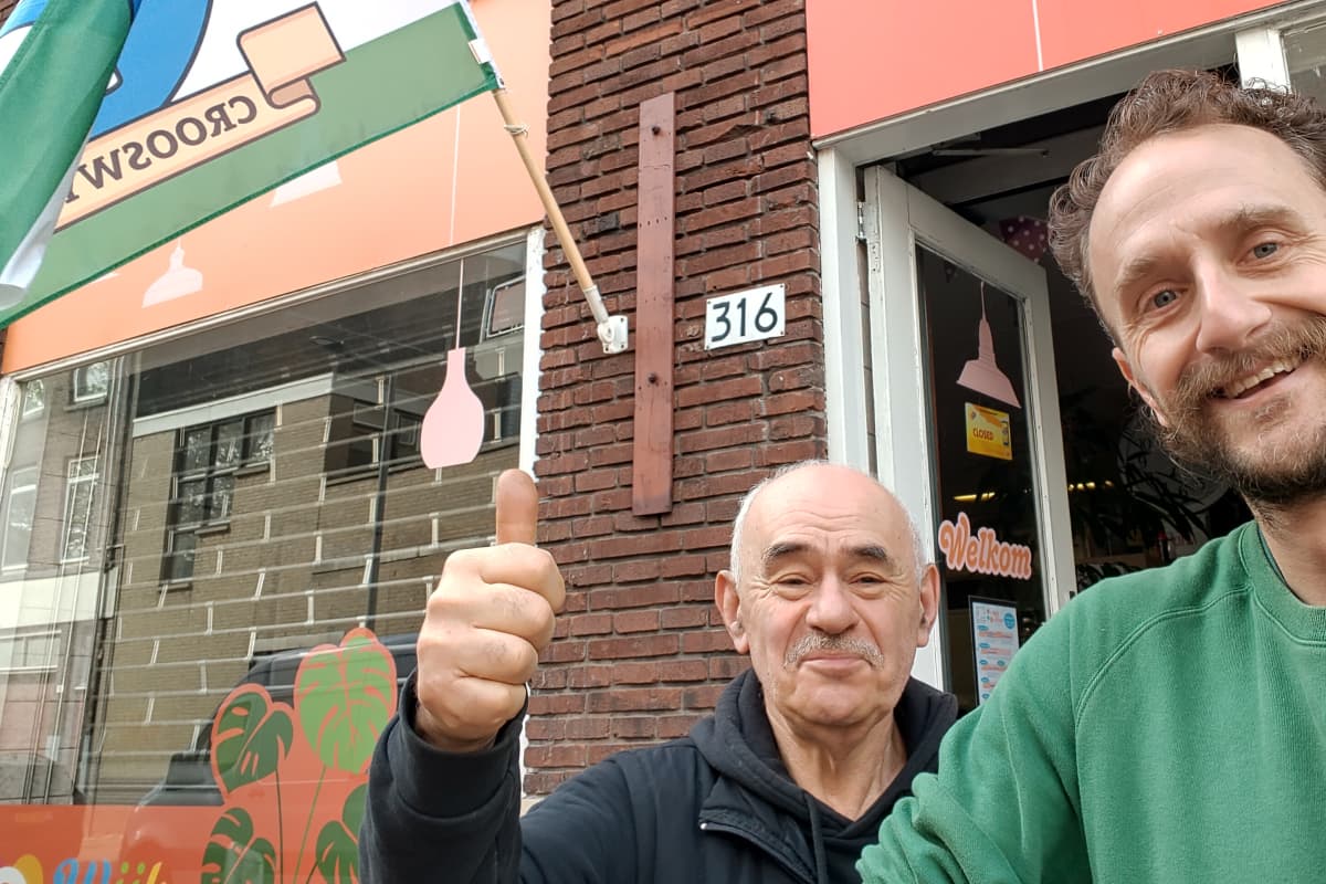 Twee mannen voor Huiskamer Crooswijk, een van hen met een duim omhoog
